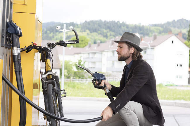 Homem reabastecendo uma bicicleta motorizada em um posto de gasolina — Fotografia de Stock