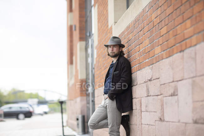 Портрет человека, прислонившегося к стене с руками в карманах — стоковое фото