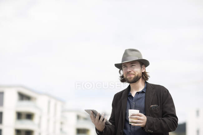 Портрет мужчины, стоящего на улице с чашкой кофе и цифровой табличкой — стоковое фото