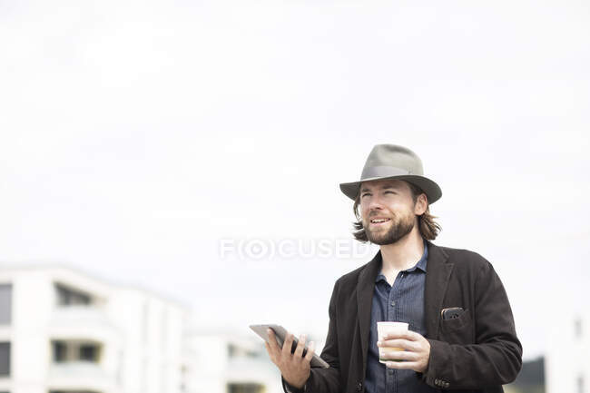 Portrait of a man standing outdoors holding a cup of coffee and digital tablet — Stock Photo
