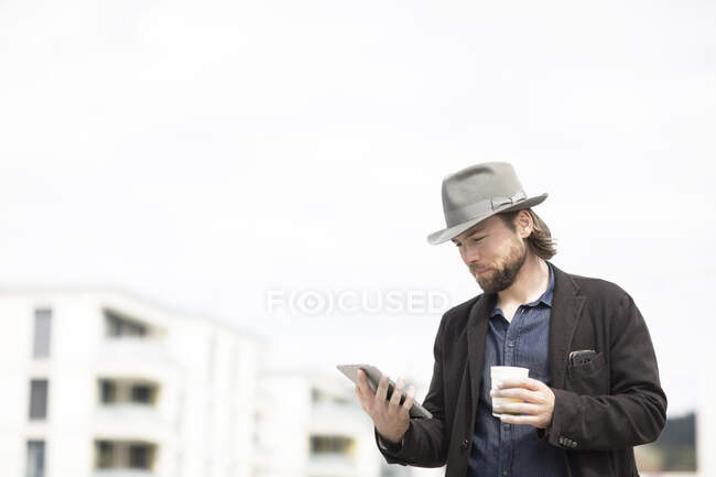 Retrato de un hombre parado al aire libre sosteniendo una taza de café y una tableta digital - foto de stock
