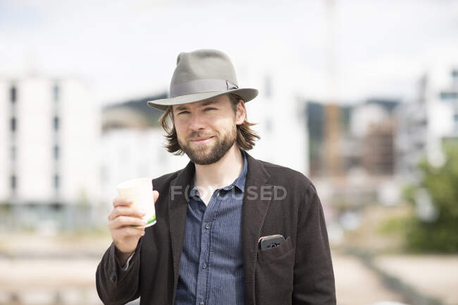 Retrato de un hombre sonriente parado al aire libre con una bebida caliente - foto de stock