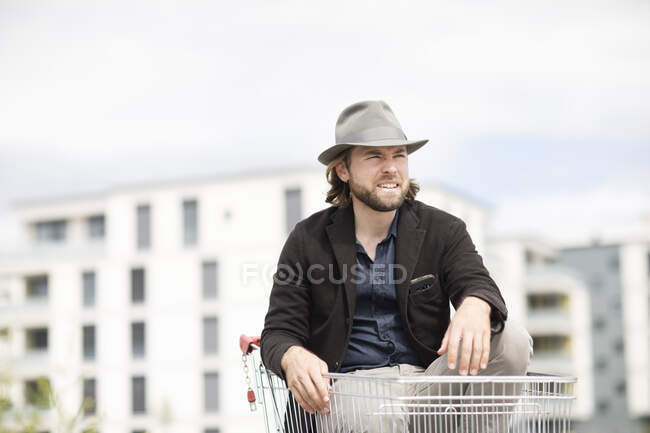 Retrato de un hombre sonriente sentado en un carrito de compras - foto de stock