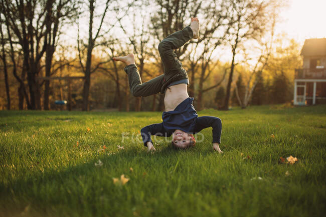 Engraçado menino de pé na cabeça no gramado verde — Fotografia de Stock
