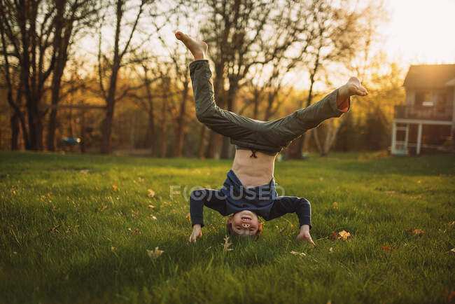 Смішний маленький хлопчик стоїть на голові на зеленому газоні — стокове фото