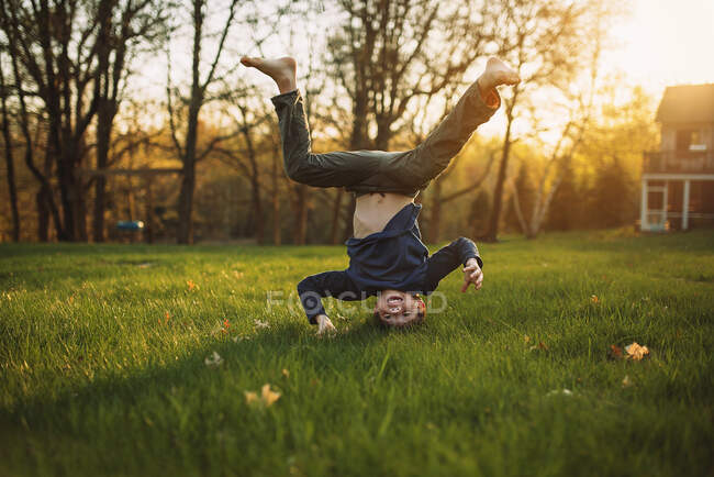Смешной маленький мальчик стоит на голове на зеленой лужайке — стоковое фото