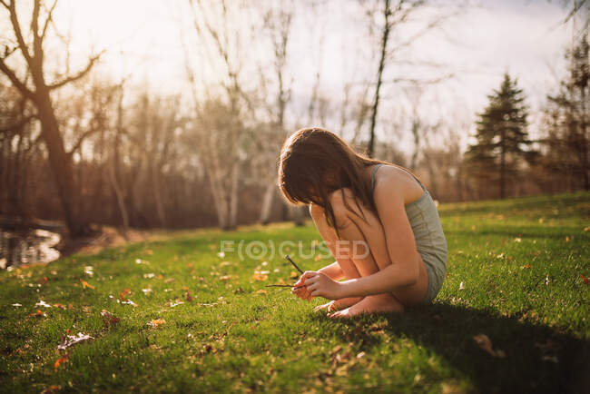 Chica sentada en el césped mirando ramitas, Estados Unidos - foto de stock