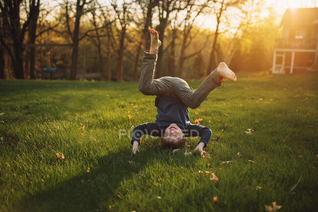 Funny little boy standing on head on green lawn — Stock Photo