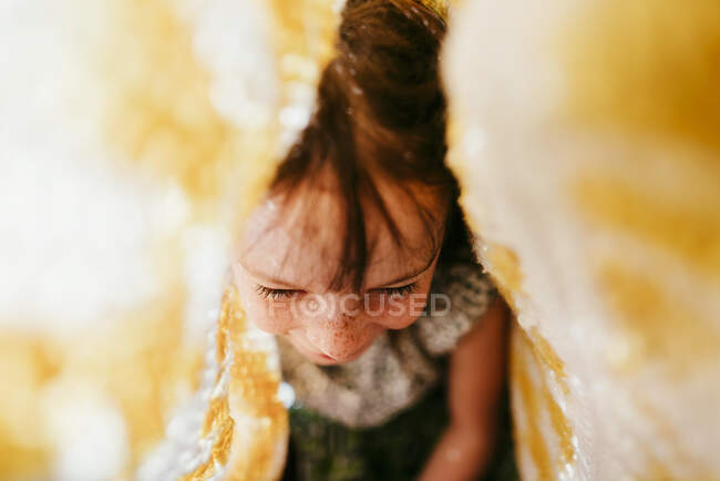 Вид зверху усміхненої дівчини з веснянками, покритими тканиною і сонячними променями на обличчі — стокове фото