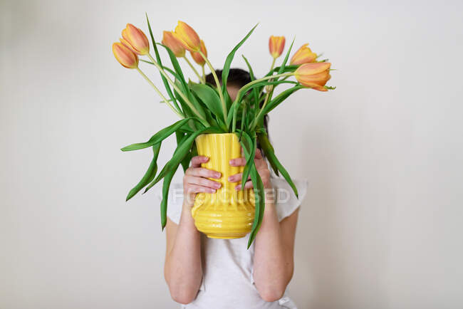 Menina bonito escondendo atrás vaso de tulipas laranja — Fotografia de Stock