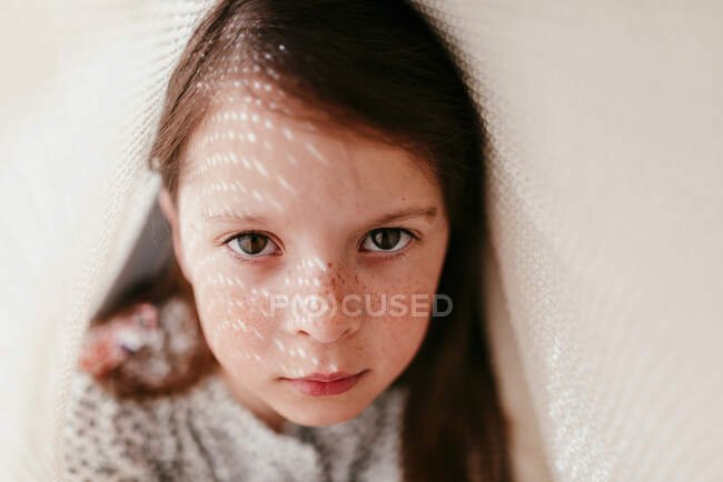 Retrato de niña con pecas cubiertas de tela y rayos de sol en la cara - foto de stock