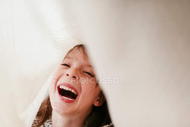 Niña riendo con pecas cubiertas de tela y rayos de sol en la cara - foto de stock