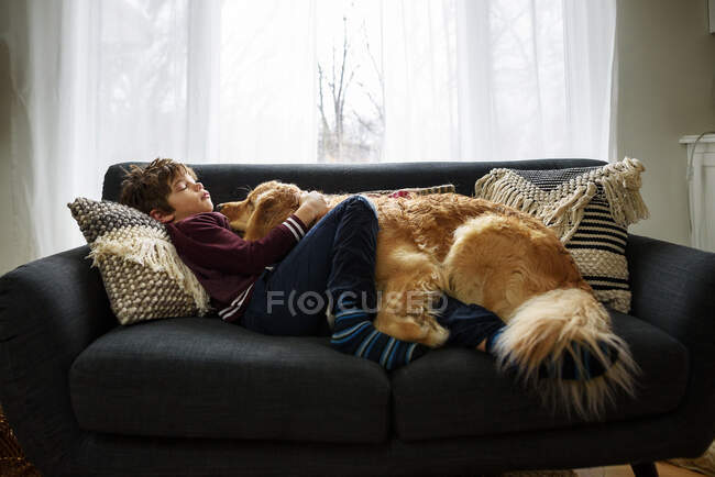 Хлопчик обіймається з собакою на дивані у вітальні — стокове фото