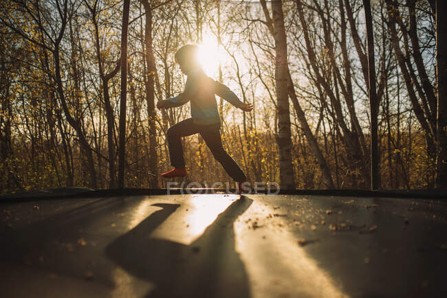 Силует хлопчика на батуті на заході сонця — стокове фото