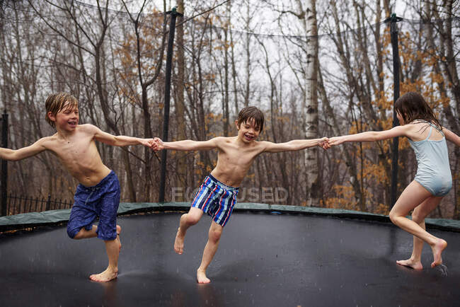 Трое детей прыгают на батуте под дождем — стоковое фото