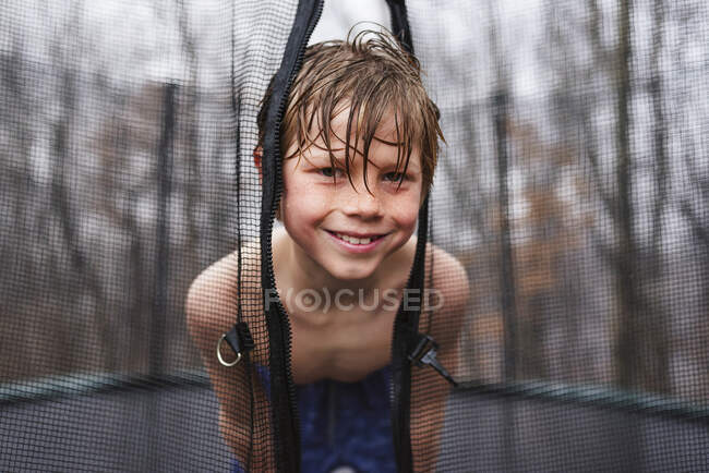 Retrato de niño mojado y feliz jugando en una cama elástica bajo la lluvia - foto de stock