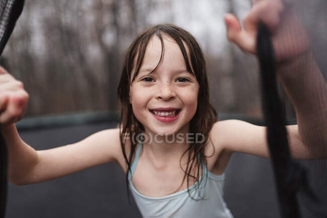 Chica sonriente jugando en un trampolín bajo la lluvia, Estados Unidos - foto de stock