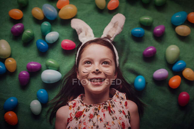 Overhead portrait of young girl wearing bunny ears surrounded by Easter eggs — Stock Photo