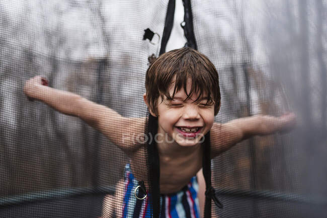 Happy boy playing on a trampoline in the rain, United States — Stock Photo
