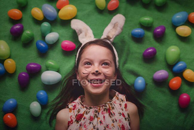 Портрет дівчини в вухах кролика, що лежить на підлозі в оточенні великодніх яєць — стокове фото