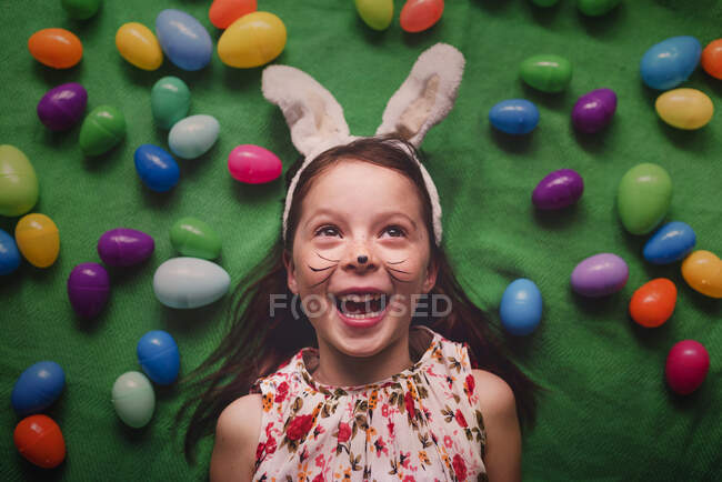 Портрет девушки с кроличьими ушами, лежащей на полу в окружении пасхальных яиц — стоковое фото