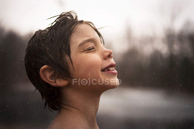 Retrato de un niño sonriente de pie bajo la lluvia - foto de stock