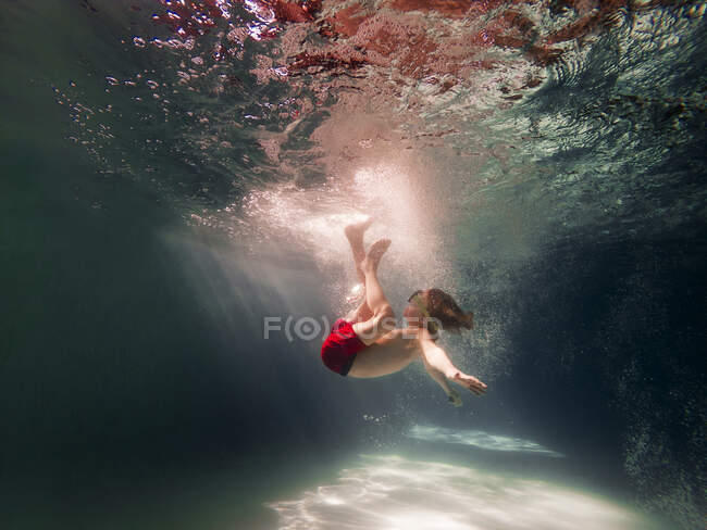Niño nadando bajo el agua en una piscina - foto de stock
