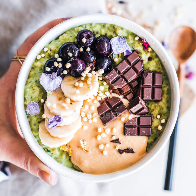 Woman holding a Matcha green tea oatmeal bowl with peanut butter, chocolate, banana and blueberries — Stock Photo