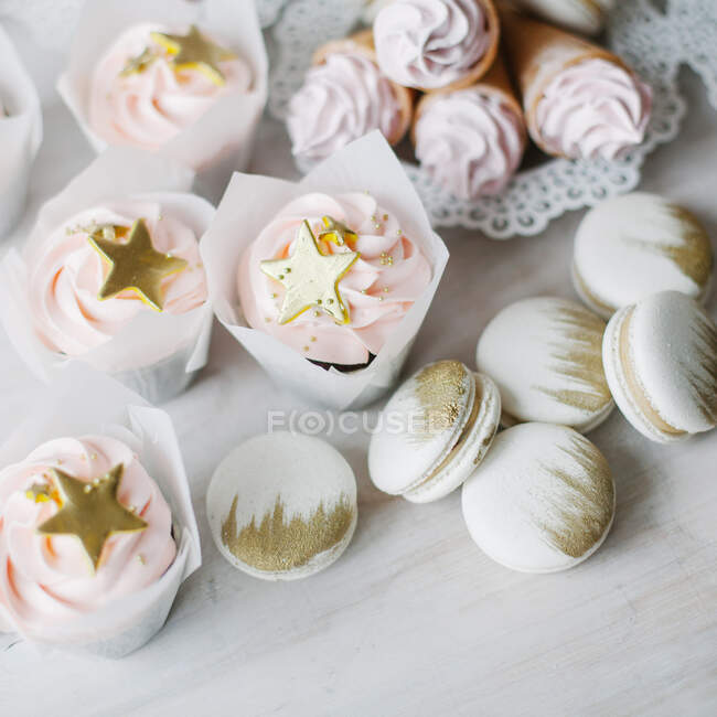 Cupcakes, waffle cones with whipped cream and macaroons with gold colored decorations — Stock Photo