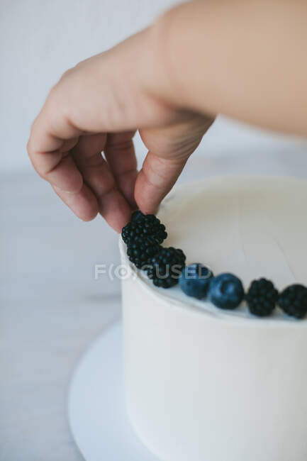 Woman decorating a cake with blueberries and blackberries — Stock Photo