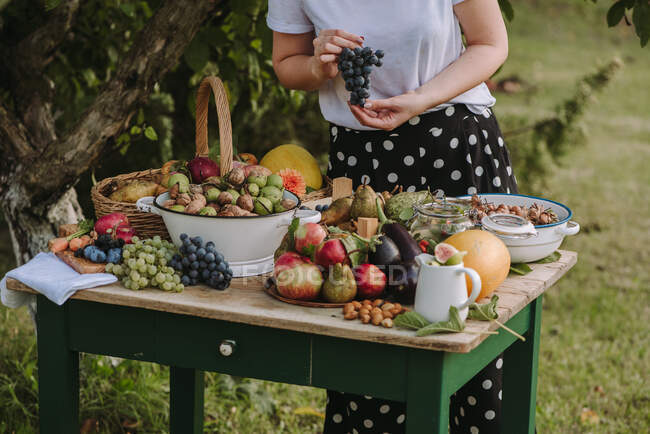 Woman standing by a table with fruit and vegetables holding a bunch of grapes, Serbia — Stock Photo