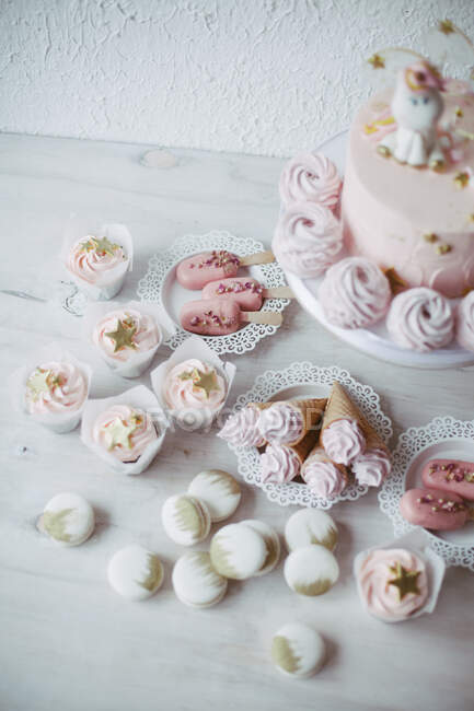 Pastel de cumpleaños unicornio con cupcakes, conos de gofre con crema, pasteles de helado y macarrones - foto de stock