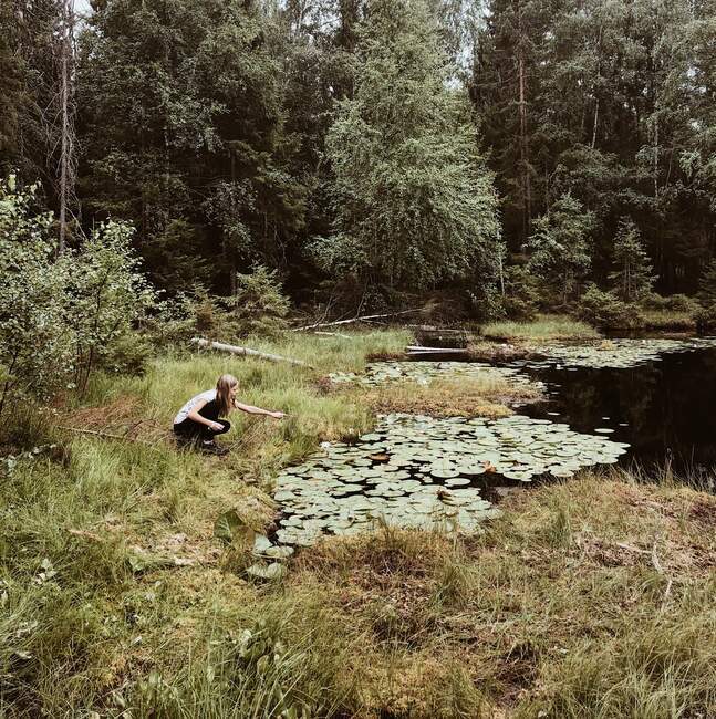 Girl crouching by a river holding a stick, Norway — Stock Photo