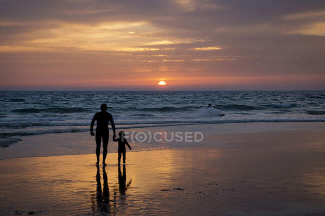 Silueta de padre e hijo cogidos de la mano en la playa al atardecer, Tarifa, Cádiz, Andalucía, España - foto de stock