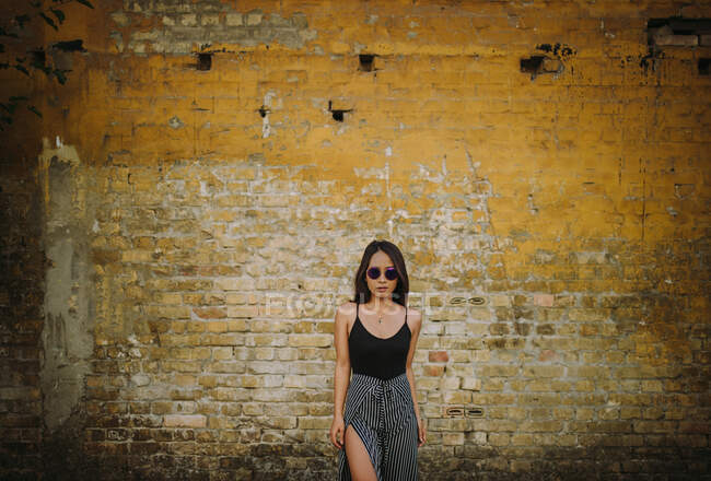 Стильная азиатская молодая женщина, стоящая перед старой кирпичной стеной — стоковое фото