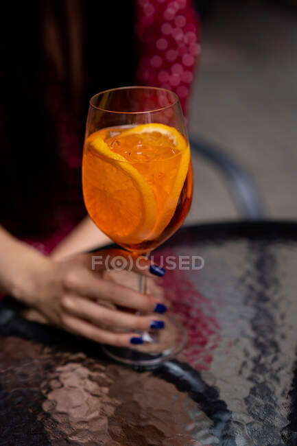 Женщина, сидящая за столом и держащая коктейль из аперола — стоковое фото