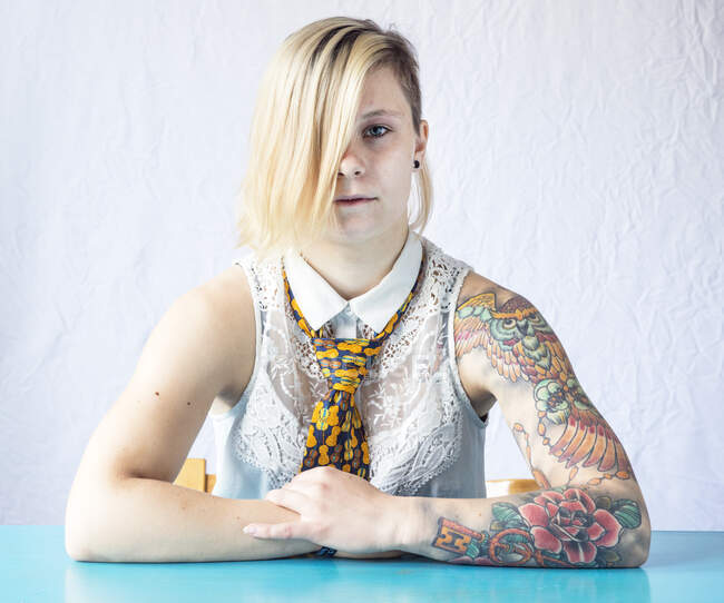 Portrait of a woman with a sleeve tattoo sitting at a table — Stock Photo