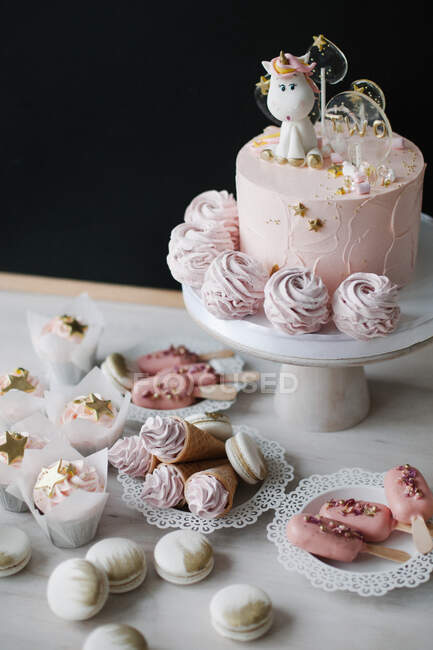 Bolo de aniversário de unicórnio com cupcakes, cones de waffle com creme, gelados e macaroons — Fotografia de Stock