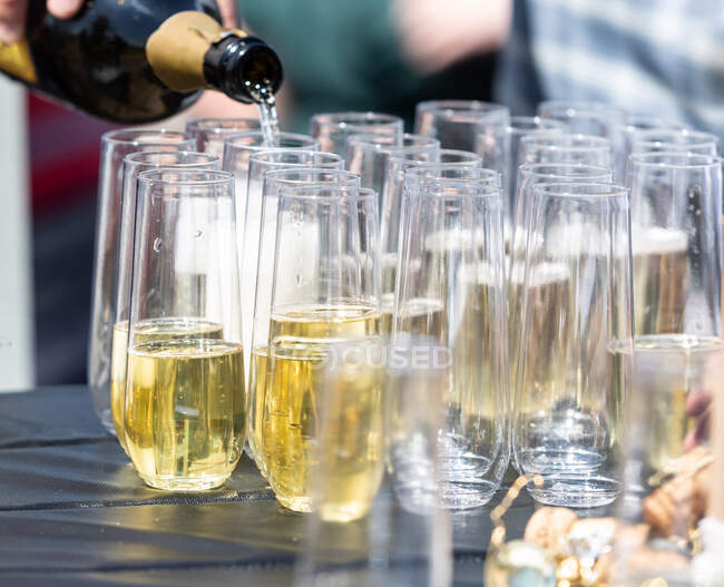 Persona que vierte champán en copas en una fiesta en el jardín - foto de stock