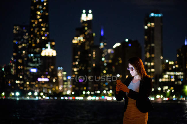 Mujer usando su teléfono móvil con el horizonte de la ciudad detrás de ella, Chicago, Illinois, Estados Unidos - foto de stock