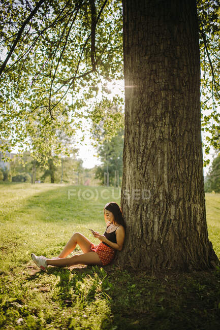 Mulher sentada debaixo de uma árvore olhando para seu telefone celular, Sérvia — Fotografia de Stock