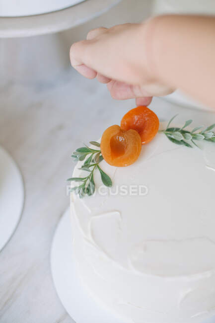Woman decorating a cake with peaches and leaves — Stock Photo