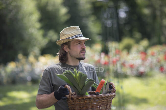 Retrato de um homem de pé em um jardim carregando uma cesta cheia de equipamentos de jardinagem, Alemanha — Fotografia de Stock