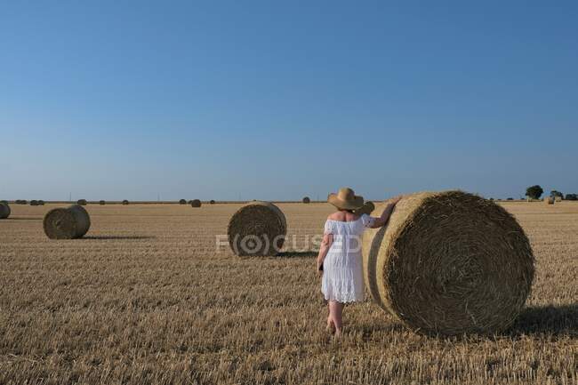 Mujer de pie en un campo apoyado sobre un heno Bale, Francia - foto de stock