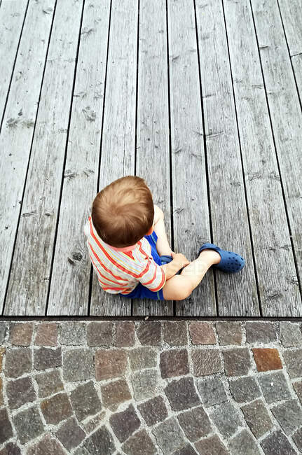 Вид сверху на мальчика, сидящего на деревянной террасе, Сардиния, Италия — стоковое фото