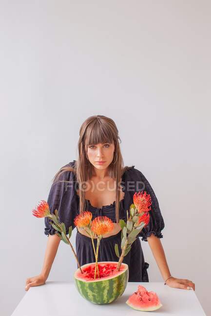 Woman standing by an arrangement of protea flowers in a watermelon — Stock Photo