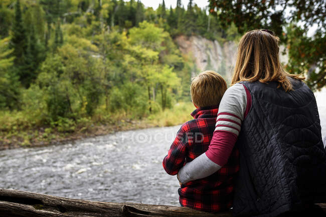 Madre e hijo sentados en un tronco de árbol mirando a la vista, Estados Unidos - foto de stock