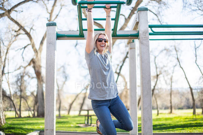 Woman hanging from monkey bars in a playground, United States — Foto stock