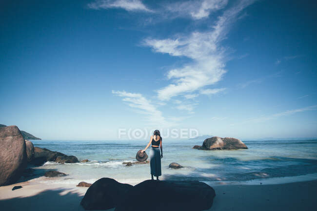 Жінка стоїть на пляжі і тримає сонцезахисний капелюх Сейшельські острови. — стокове фото