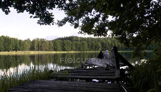 Pareja sentada en un embarcadero de madera, Moletai, Lituania - foto de stock